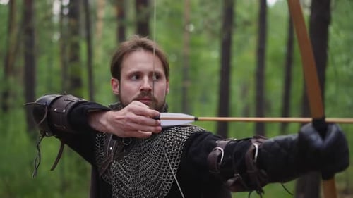Concentrated Bearded Archer Shoots Bow in Green Wood Closeup