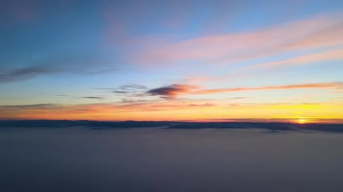 Aerial View of Colorful Sunset Over White Dense Foggy Clouds Cover with Distant Dark Silhouettes of