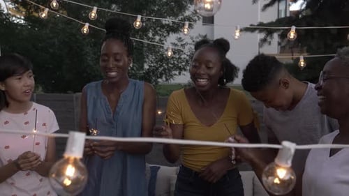 Diverse Group Celebrates Outdoors with Sparklers and String Lights