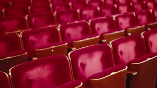 Slow tracking movement over worn empty red velvet theatre audience chairs