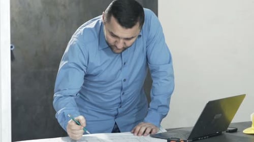Young architect at new home works on laptop with blueprints by table