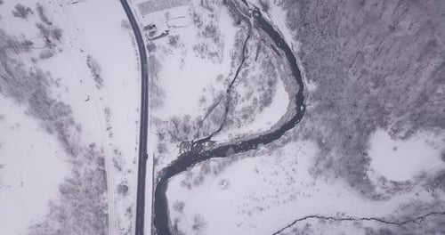Aerial footage of cars passing by a road. A frozen river is on the right side of the road, alongside