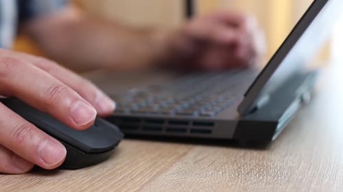 15Close-up of hands using a laptop keyboard and mouse on a wooden desk. Work, internet browsing, and