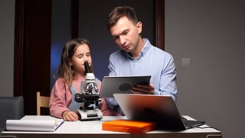 Girl using Microscope with Man holding Tablet