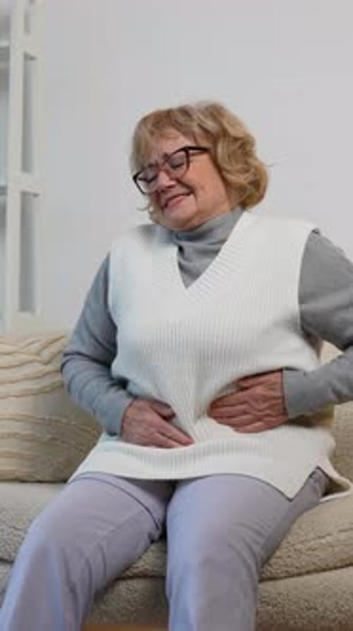 Senior Woman Holding Stomach While Sitting on Couch