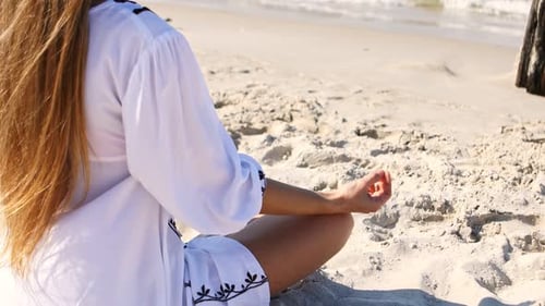 Jeune femme aux cheveux roux en haut blanc se relaxant et méditant sur une plage exotique pendant les vacances