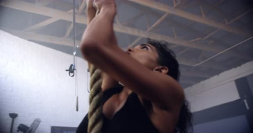 An attractive young woman climbing a rope at the gym