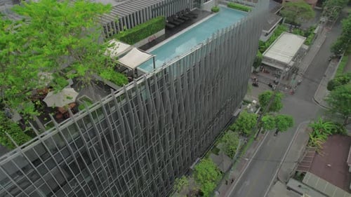 Drohne, die um ein Gebäude in Bangkok, Thailand, fliegt. Dachterrasse mit Pool, Tischen und einigen Bäumen.