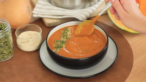 Eine Frau rührt Kürbissuppe mit einem Löffel in einen Teller. Herbstmenü-Video