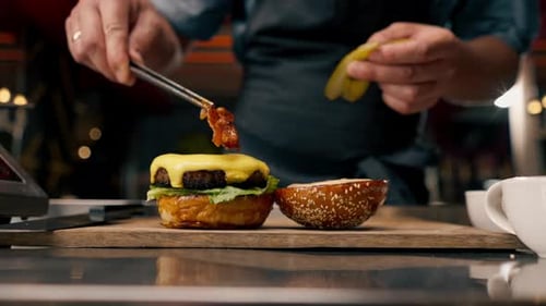 A close-up of a chef preparing a burger with beef patty with vegetables and cheese in the kitchen