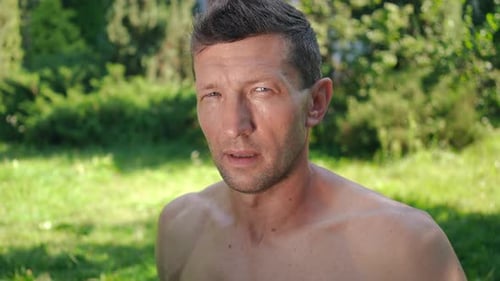 Zoom in to Exhausted Sweating Sportsman Posing Outdoors on Sunny Day Wiping Perspiration with Hand