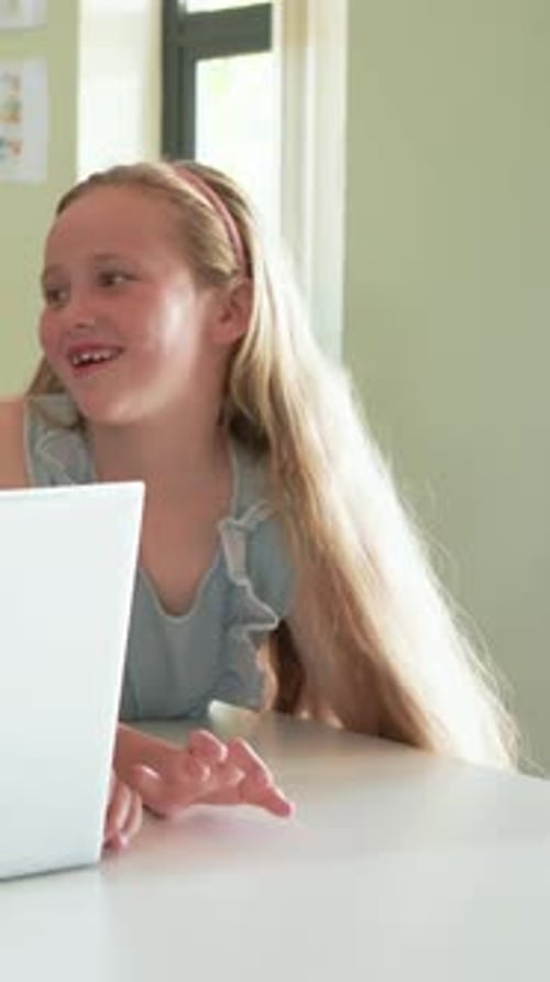 Girl and boy leaning in, tapping white laptop, creating learning graphics around screen for lesson