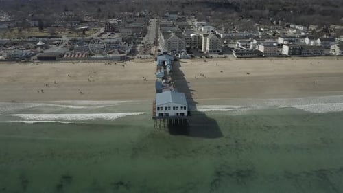 Drone shot, of a pier on the beach, flying to the right and panning up.