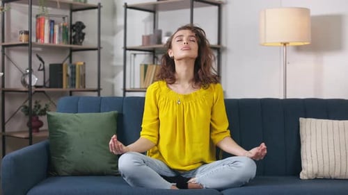 Young Woman Meditating on Sofa at Home