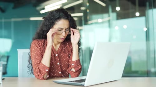 Exhausted, overworked woman office worker sitting in the workplace with severe headache massaging