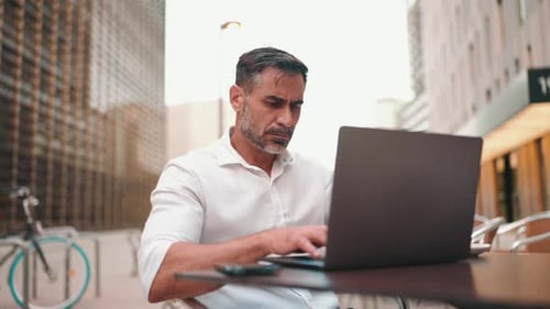 Mature businessman user on laptop pc computer sit at cafe outdoors