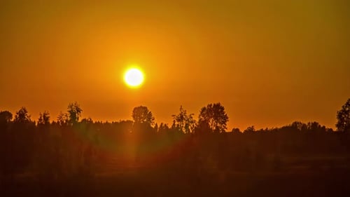 Ein heller, feuriger Sonnenuntergang über dem Land färbt sich in der Abenddämmerung orange - Zeitraffer