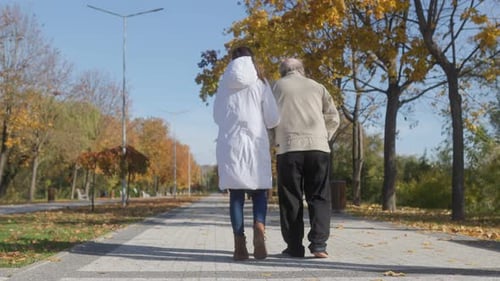 Senior Care in Autumn Park Back View of Elderly Man and Nurse Walking