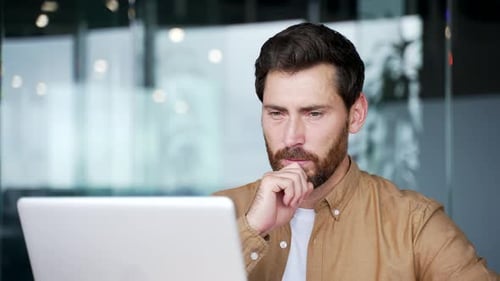 Ernsthafter, nachdenklicher Geschäftsmann, der über Problemlösungen nachdenkt, während er am Laptop sitzt