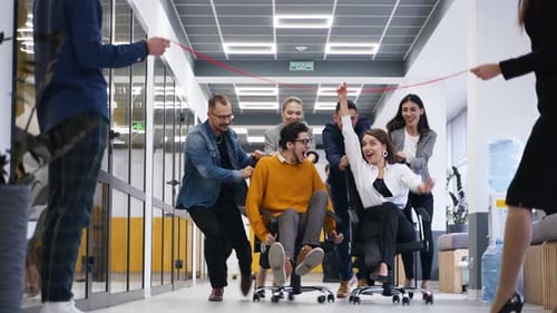 Cheerful People Have Fun During Workday Break Two Teams Compete in Chair on Wheels Racing in Office