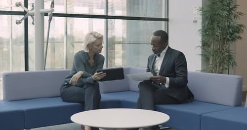 Business people in office meeting in modern lobby on sofa using digital tablet