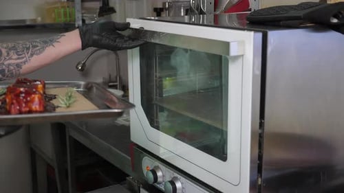 The Chef Puts a Baking Tray with Pickled Pork Ribs in the Oven in the Restaurant
