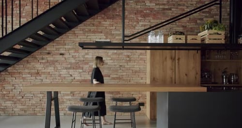 Woman walk near table with wooden countertop and bar stools at modern apartment