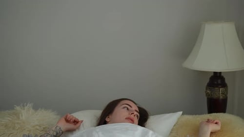Gros plan La fille se réveille, s'assoit dans son lit et se rend compte qu'elle a trop dormi, réalisant cela qu'elle regarde