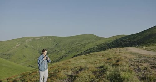 A Young Woman in Casual Attire Captures the Breathtaking Scenery of Rolling Mountain Landscapes