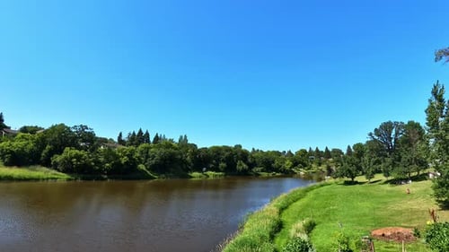 Ruhige Flusslandschaft mit üppigen grünen Wiesen, von Bäumen gesäumten Ufern und klarem blauem Himmel.