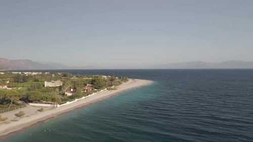 Aerial drone forward shot over crystal clear turquoise waters along the beach with coastal houses