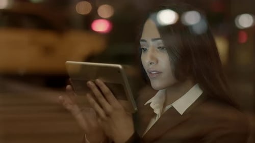 In a Modern Office a Businesswoman Reads Intently From Her Tablet at Night with Reflection