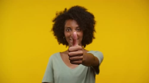 Smiling Woman Gives Thumbs Up on Yellow Background