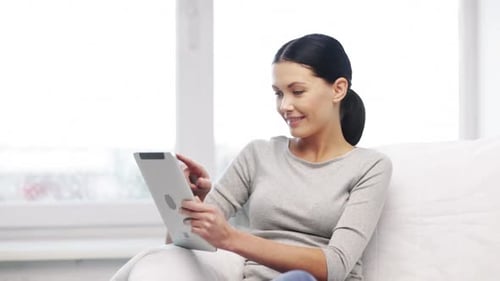 Woman Smiles, Using Tablet While Relaxing on Couch