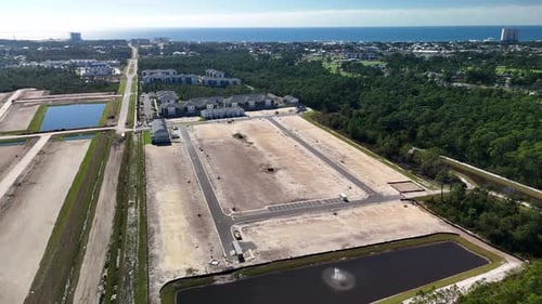 A Developing Neighborhood With Land Plots, Buildings, and a Retention Pond, Set Against Greenery and