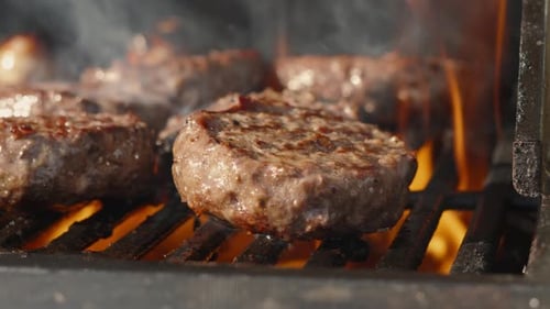 Nahaufnahme von flammengegrillten brutzelnden Barbecue-Rinderburgern in Zeitlupe