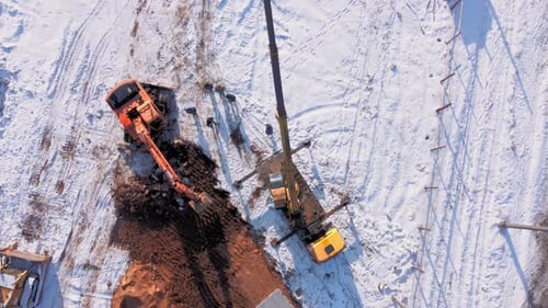 aerial top down view. Excavator loads dump truck with earth on winter day.