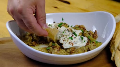 chef dips bread into a dish with yogurt sauce in a plate