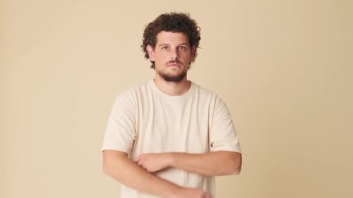 Man crossing his arms, looking at the camera with smile isolated on beige background in studio