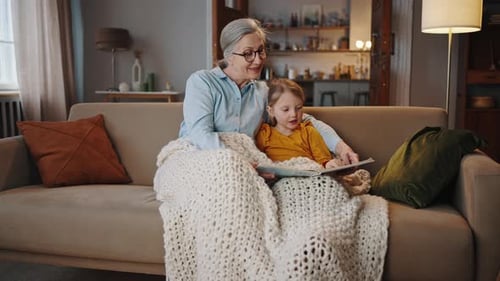 Grandmother and Granddaughter Reading a Book on Couch