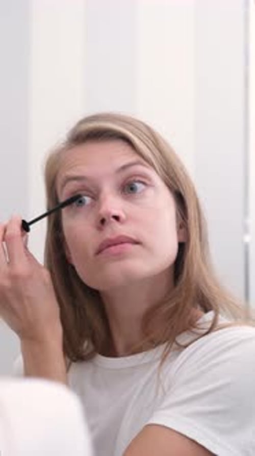 Young Woman Applies Mascara in Bathroom Mirror