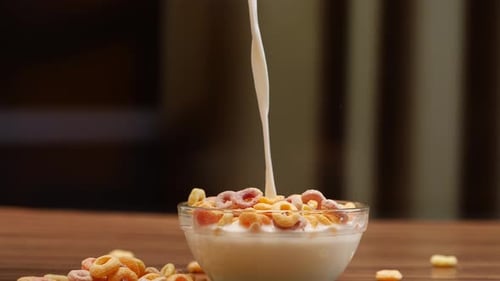 Leche vertida en un tazón de cereales con un montón de cereales sobre una mesa