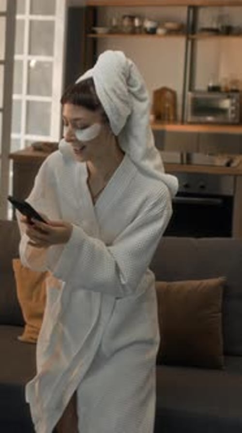 Young Woman in Robe Texts on Phone at Home