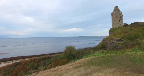 Ruins of ancient Scottish castle on lakefront headland. Aerial forward ascendent