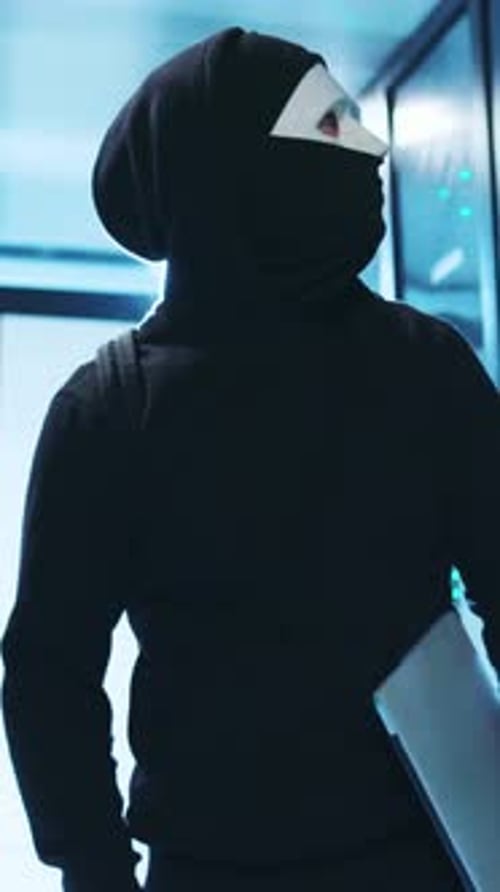 Masked Hacker with Laptop in Dark Server Room