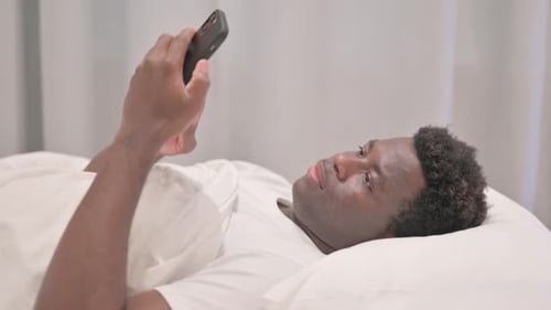Side View of African American Man using Smartphone in Bed