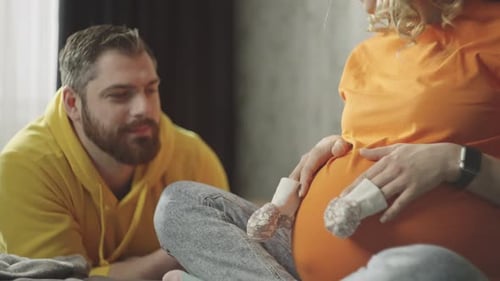 Pregnant Woman and Partner Holding Baby Shoes