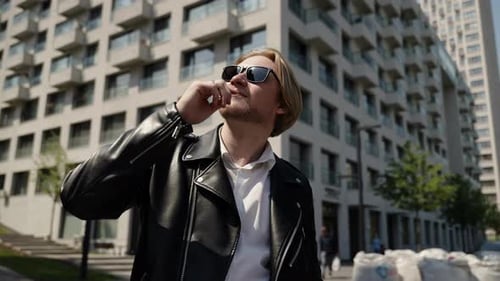 A Man in a Leather Jacket Poses for the Camera Against the Backdrop of Beautiful Architecture The