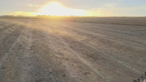A self-propelled agricultural sprayer operates across a vast, dusty plowed field at sunset, demonstr