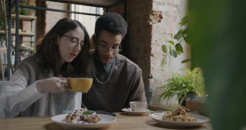 Girl and Guy Happy Couple Looking at Smartphone Screen Talking and Drinking Coffee in Cafe